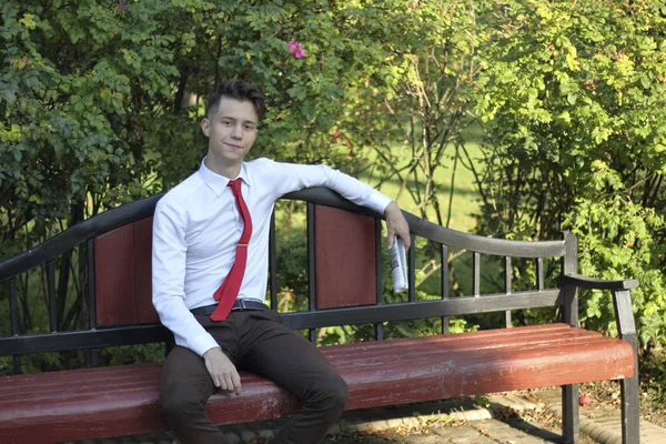 Um jovem elegantemente vestido senta-se em um banco do parque e segura um jornal em suas mãos. olha para longe com um sorriso . — Fotografia de Stock