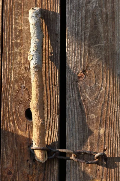 A porta do antigo celeiro está fechada numa corrente. Uma vara de madeira é inserida no loop . — Fotografia de Stock