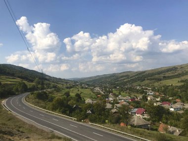 Transcarpathia'nın dağ manzaraları. Orman, çimenlerle kaplı tepeler arasında giden bir yol. Uzakta, köy görünür.
