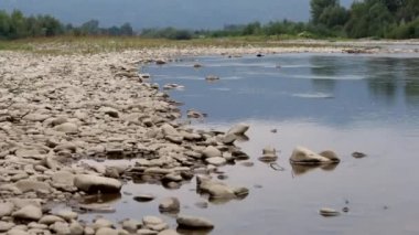 Bir dağ nehrinin su akıntısı. Vadide sakince akar. Kayalık kıyılar görülebilir. Dağ ufkunda.