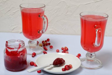 Ev yapımı boşluklar. Açık bir kavanozda kızılcık reçeli ve kızılcık suyu ile bardak. Bir tabak üzerinde reçel ile bir çay kaşığı. Birkaç çilek yüzeye serpilir.