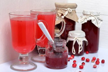 Ev yapımı boşluklar. Kızılcık suyu ile kavanoz ve bardak kızılcık reçeli. Bir açık olabilir, bir çay kaşığı vardır. Birkaç çilek yüzeye serpilir.