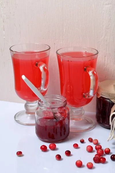 Homemade blanks. Cranberry jam in jars and glasses with cranberry juice. One can is open, it has a teaspoon. Several berries are scattered on the surface.