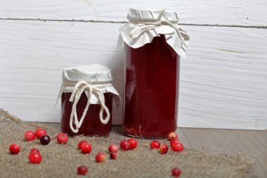 Ev yapımı boşluklar. Kızılcık suyu ile kavanoz ve bardak kızılcık reçeli. Birkaç çilek yüzeye serpilir.