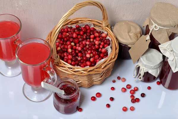 Homemade blanks. Cranberry jam in jars and glasses with cranberry juice. One can is open, it has a teaspoon. Several berries are scattered on the surface.