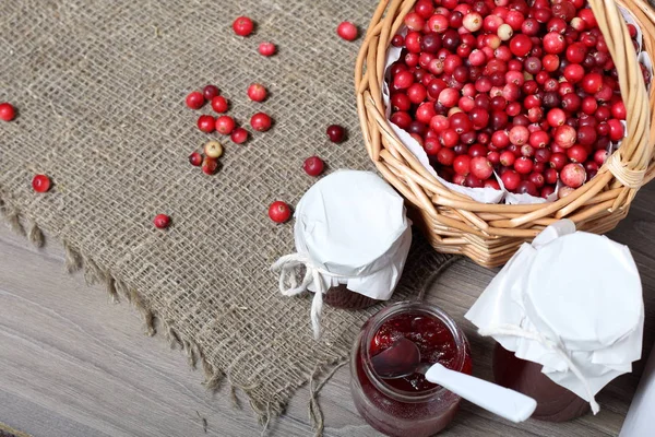 Homemade preserves, cranberry jam in jars. One can is open, it has a teaspoon. Several berries are scattered on the surface.