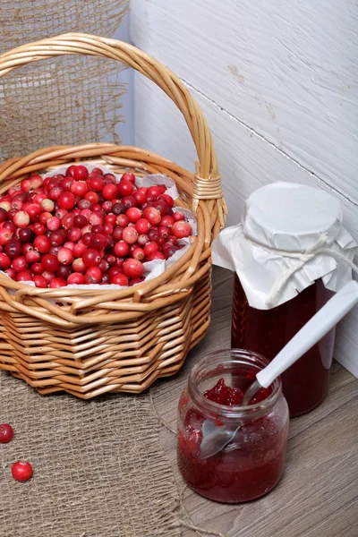 Homemade preserves, cranberry jam in jars. One can is open, it has a teaspoon. Several berries are scattered on the surface.