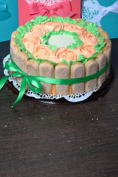 Gâteau éponge au fromage à la crème, décoré de biscuits Savoiardi. Sur le côté, enveloppé dans un ruban attaché à un arc. Près d'une carte de vœux . — Photo