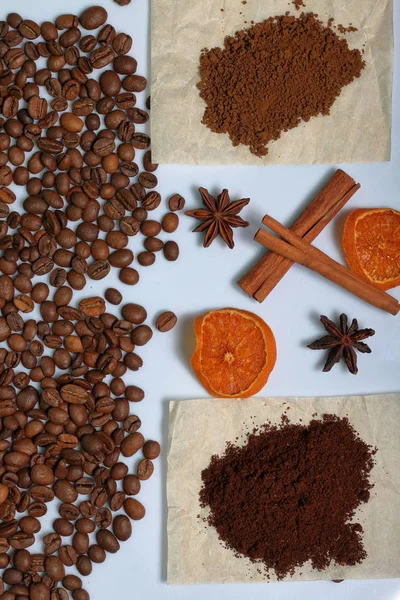 Grains of coffee and slices of dried oranges are scattered on the surface of the table. Cinnamon sticks and anise are also visible. A few servings of ground coffee. World Coffee Day.