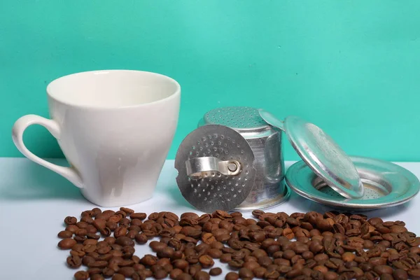 Une tasse de café avec une cafetière vietnamienne. Grains de café dispersés à proximité sur la surface de la table. Journée mondiale du café . — Photo