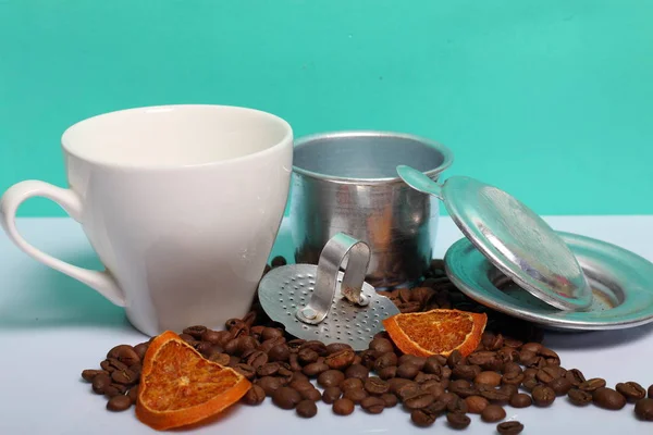 A cup of coffee with a Vietnamese coffee maker. Nearby on the surface of the table are grains of coffee and slices of dried oranges. World Coffee Day.
