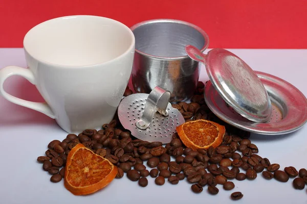 A cup of coffee with a Vietnamese coffee maker. Nearby on the surface of the table are grains of coffee and slices of dried oranges. World Coffee Day.