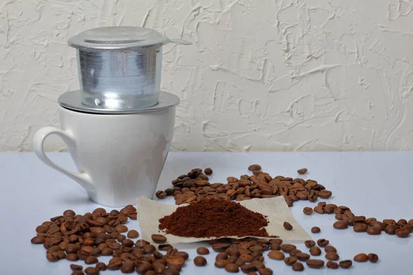 Una taza de café con una cafetera vietnamita. Cereales de café y un poco de café molido se encuentran dispersos en la superficie de la mesa. Día Mundial del Café . — Foto de Stock