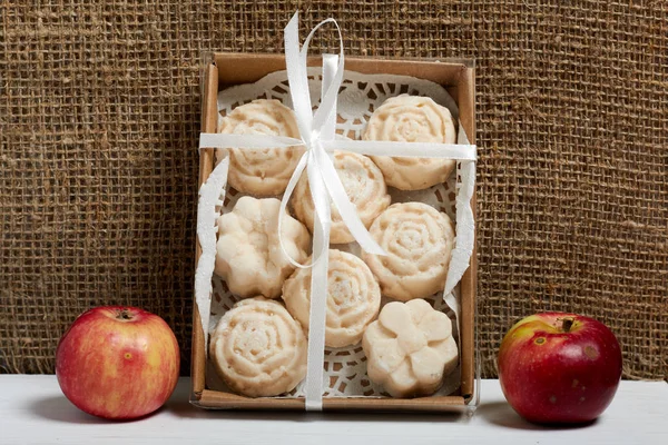Apple puree marshmallows in a gift box. Tied with a ribbon tied to a bow. Nearby are fresh apples.