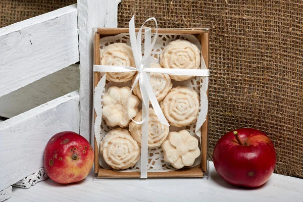 Apple puree marshmallows in a gift box. Tied with a ribbon tied to a bow. Nearby are fresh apples.