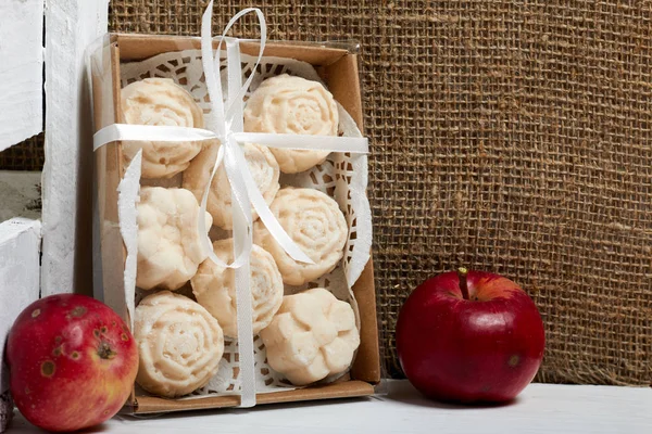 Apple puree marshmallows in a gift box. Tied with a ribbon tied to a bow. Nearby are fresh apples.