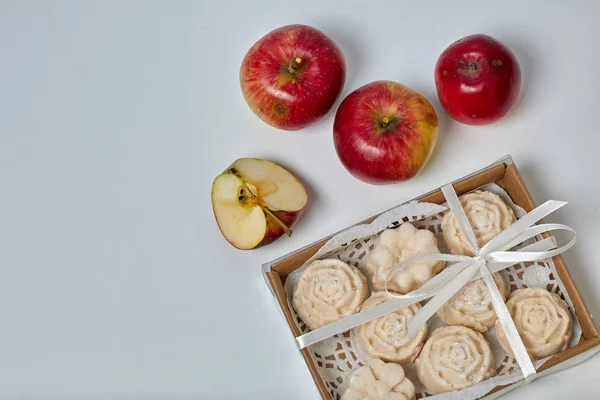 Apple puree marshmallows in a gift box. Tied with a ribbon tied to a bow. Nearby are fresh apples.