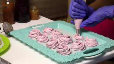 Bir kadın hamur torbasıyla marşmelov yapar. Şekerlemeler tepsiye konur..