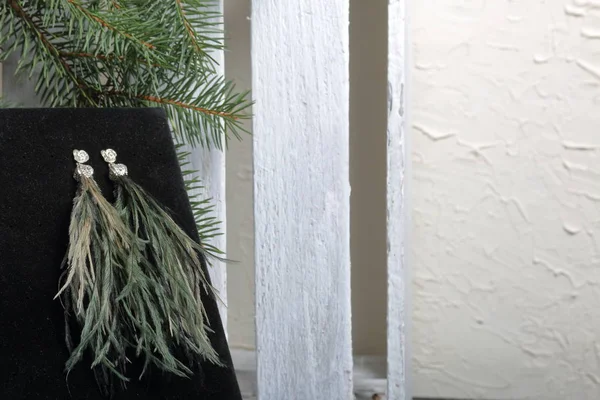 Ostrich feather brush earrings. On black velvet. Against the background of a fir branch and a white wooden box.