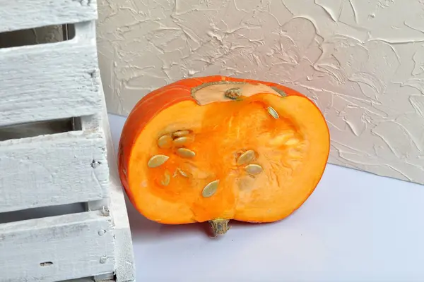 La moitié d'une citrouille orange repose sur une surface blanche. A proximité se trouve une boîte de planches en bois peintes en blanc . — Photo