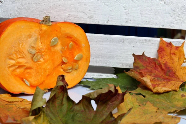 Ein halber orangefarbener Kürbis liegt auf einer weißen Fläche. In der Nähe steht eine Kiste mit weiß bemalten Holzbrettern. Dekoriert mit bunten Herbstblättern. — Stockfoto