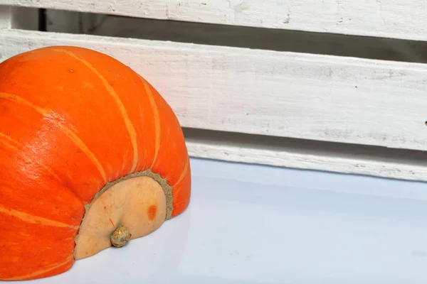 Half an orange pumpkin lies on a white surface. Nearby is a box of white painted wooden boards. — Stock Photo, Image