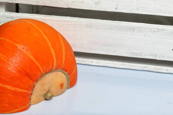 La moitié d'une citrouille orange repose sur une surface blanche. A proximité se trouve une boîte de planches en bois peintes en blanc . — Photo