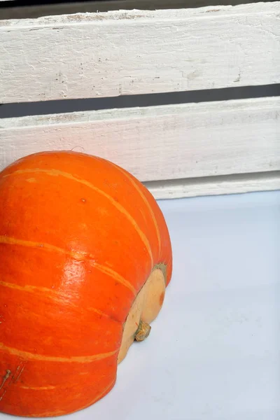 Половина оранжевой тыквы лежит на белой поверхности. Рядом находится коробка из белых окрашенных деревянных досок . — стоковое фото