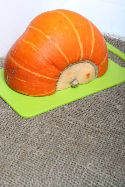 La mitad de una calabaza naranja yace en una tabla de cortar. La superficie está cubierta con tela de lino grueso . — Foto de Stock