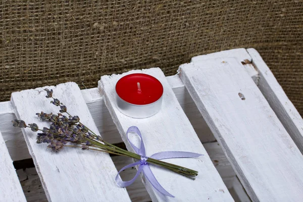 Un mazzo di lavanda legato a un nastro, giace su una scatola di legno. Nelle vicinanze c'è una candela . — Foto Stock