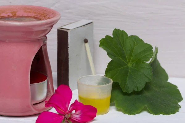 Daun dan perbungaan geranium untuk aromaterapi terletak di sebelah lampu aroma. Minyak dituangkan ke tutupnya. Apotek alami. Aromaterapi dengan minyak alam . — Stok Foto