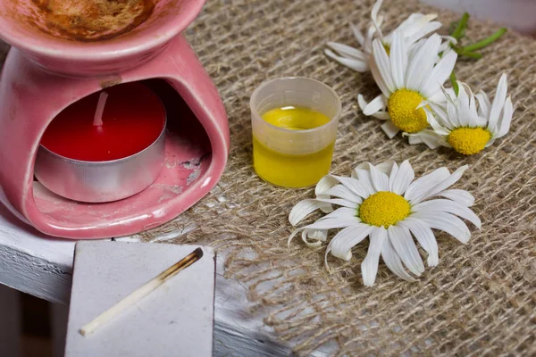 Lámpara de aroma se encuentra en una caja de madera. Cerca hay aceite en una gorra y flores de manzanilla. . — Foto de Stock