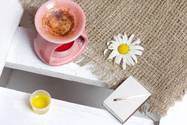 Lámpara de aroma se encuentra en una caja de madera. Cerca hay aceite en una gorra y flores de manzanilla. . — Foto de Stock