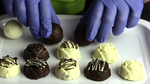 ゴム手袋の男はトレイの上に列にキャンディーを置く。白と黒のチョコレートでガラスのお菓子. — ストック動画