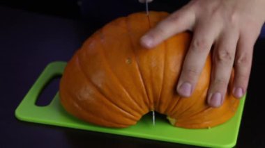 Adamın biri balkabağını kesme tahtasındaki bıçakla kesiyor. Balkabağı turuncu. Dünya Vejetaryen Günü.