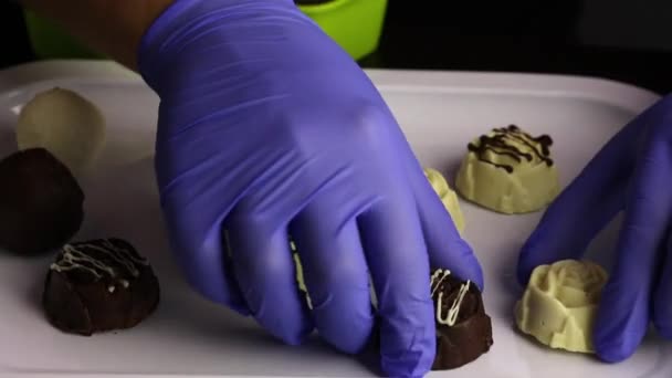 Egy gumikesztyűs férfi fehér és fekete csokoládéba mázolt cukorkát rak. Sorok a tálcán. Nemzetközi édességnap. — Stock videók