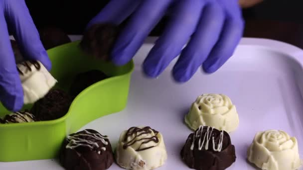 Чоловік у гумових рукавичках перетинає шоколад з лотка в посудину. Глазуровані цукерки з білого і чорного шоколаду. Міжнародний день цукерок — стокове відео