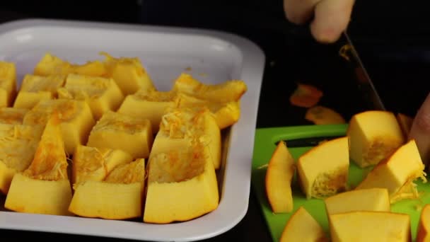 Un hombre corta una calabaza naranja en pedazos. Piezas apiladas en una bandeja. Día Mundial del Vegano . — Vídeo de stock