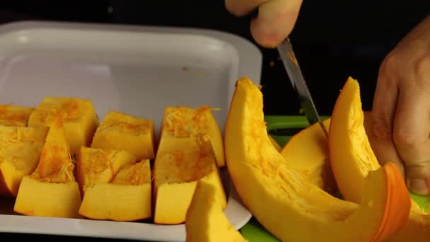 A man cuts into pieces an orange pumpkin and puts it on a tray. World Vegan Day. — Stock Video