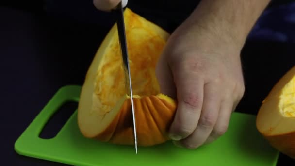 Ein Mann schneidet einen Kürbis mit einem Messer auf einem Schneidebrett. Der Kürbis ist orange. Weltveganer Tag — Stockvideo