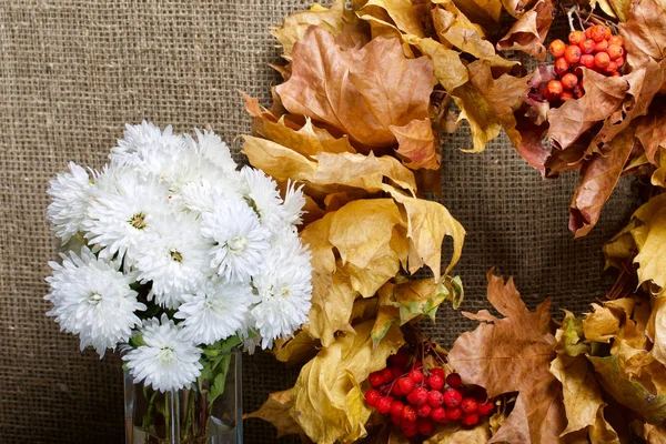 Autumn still life. Wreath of autumn leaves with mountain ash. Nearby is a bouquet of white chrysanthemums.
