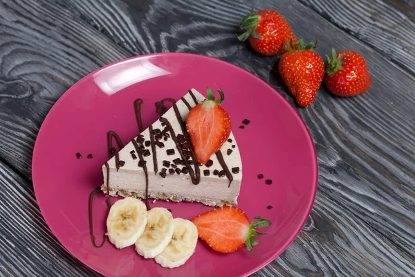 プレートの上にチーズケーキ イチゴ バナナ チョコレートが添えられています 黒と白で塗装ブラシ付きの松の板に — ストック写真