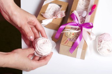 Kağıt ambalajda marşmelov ve kadın eli. Kurdelelerle ve kurumuş çiçeklerle süslenmiş. Gül şeklinde marşmelovlar. Beyaz arkaplanda.