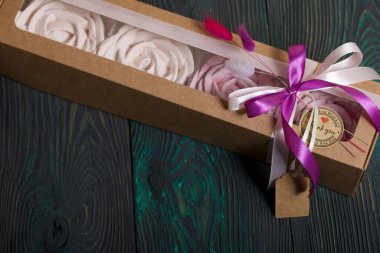 Kağıt ambalajda marşmelov. Kurdelelerle ve kurumuş çiçeklerle süslenmiş. Gül şeklinde bir Zephyr. Boyalı çam tahtalarında.