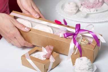 Kağıt ambalajda marşmelov ve kadın eli. Kurdelelerle ve kurumuş çiçeklerle süslenmiş. Gül şeklinde marşmelovlar. Beyaz arkaplanda.