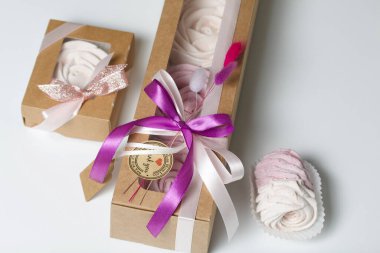 Kağıt ambalajda marşmelov. Kurdelelerle ve kurumuş çiçeklerle süslenmiş. Gül şeklinde bir Zephyr. Beyaz arkaplanda.