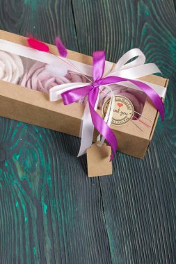 Kağıt ambalajda marşmelov. Kurdelelerle ve kurumuş çiçeklerle süslenmiş. Gül şeklinde bir Zephyr. Boyalı çam tahtalarında.