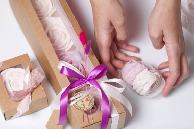 Kağıt ambalajda marşmelov ve kadın eli. Kurdelelerle ve kurumuş çiçeklerle süslenmiş. Gül şeklinde marşmelovlar. Beyaz arkaplanda.