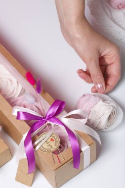 Kağıt ambalajda marşmelov ve kadın eli. Kurdelelerle ve kurumuş çiçeklerle süslenmiş. Gül şeklinde marşmelovlar. Beyaz arkaplanda.