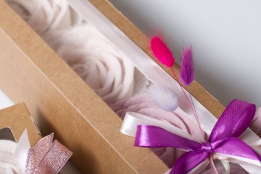 Kağıt ambalajda marşmelov. Kurdelelerle ve kurumuş çiçeklerle süslenmiş. Gül şeklinde bir Zephyr. Beyaz arkaplanda.